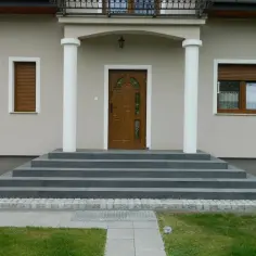 Eleganckie wejście do domu po schodach z drewnianymi drzwiami i białymi kolumnami.