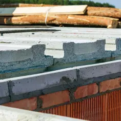 Budowa domu: strop teriva panel na ceglanym murze, w tle drewno i zbrojenie.