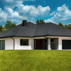 Nowoczesny dom z ciemnym dachem i garażem, otoczony zielenią. Zastanawiasz się, ile waży dom?