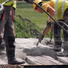 Budowlańcy w kamizelkach i kaskach wylewają beton na strop. Prawidłowe wykonanie to klucz do tego, jak dbać o świeży strop.