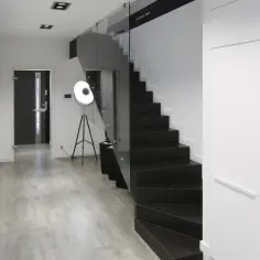Nowoczesne schody czarne z podstopniami, szklaną balustradą i minimalistycznym wnętrzem.