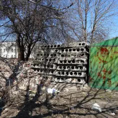 Stos płyt żerańskich, gruz i zielona, zardzewiała hala garażowa.