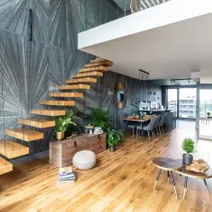 Nowoczesne szare schody drewniane unoszą się nad salonem z designerską tapetą i wygodną sofą.
