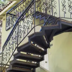 Solidne schody z metalu z ozdobną balustradą prowadzą na piętro. Obok drzwi numer 208.