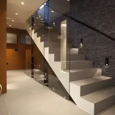 Nowoczesna klatka schodowa w domu, z białymi stopniami, szklanymi balustradami i kamienną ścianą.