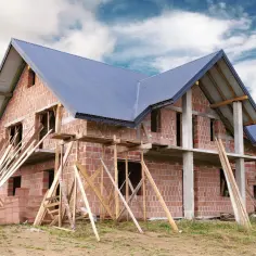 Budowa domu z cegły, porowaty materiał budowlany, z niebieskim dachem i drewnianymi rusztowaniami.