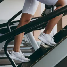 Kobieta w białych legginsach i butach sportowych wchodzi po schodach na bieżni. Czy chodzenie po schodach odchudza? Ten trening to świetny sposób na spalanie kalorii.