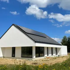 Nowoczesny dom prefabrykowany betonowy z panelami słonecznymi na dachu, otoczony zielenią i polnymi kwiatami.