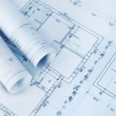 Zrolowane dokumenty z projektem architektoniczno budowlanym leżą na szczegółowych planach pomieszczeń i wymiarach.