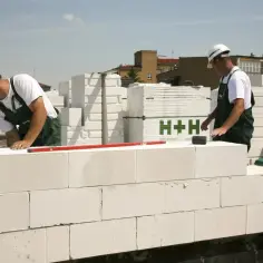 Dwóch budowlańców w kaskach murowanych z białych pustaków na placu budowy.