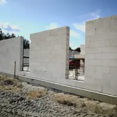 Budowa domu z pustaka beton komórkowy. Ściany wznoszą się na fundamencie, w tle drzewa i błękitne niebo.