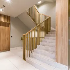 Drewniana ściana lamelowa i złota balustrada schodów to świetny pomysł na ścianę przy schodach. Eleganckie wnętrze.