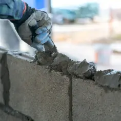 Budowlaniec nakłada zaprawę do betonu komórkowego na bloczki, tworząc solidną ścianę.