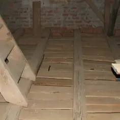 Drewniana konstrukcja podłogi na strychu, przygotowana do naprawy stropu drewnianego. Widoczne belki, deski i drabina.