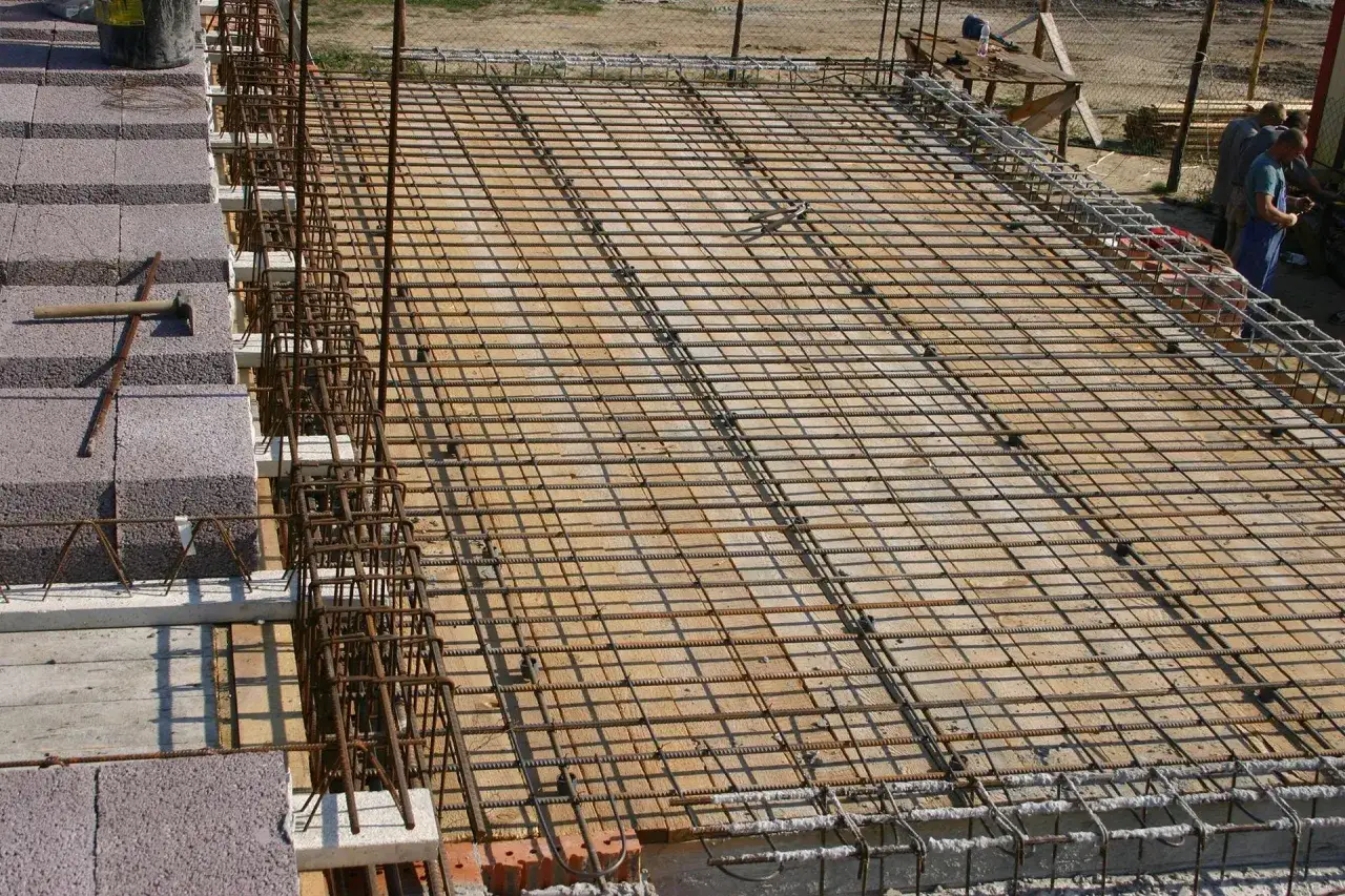 Siatka zbrojeniowa na stropie na belkach stalowych, przygotowana do zalania betonem. Widać elementy konstrukcyjne i materiały budowlane.