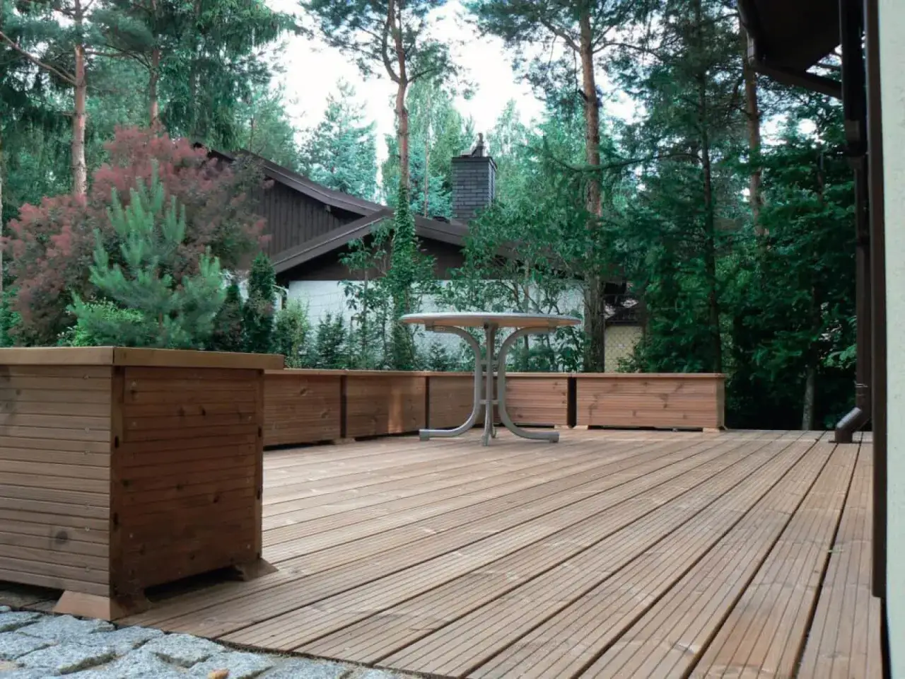 Drewniany taras z donicami i stolikiem. Zastanawiasz się, ile kosztuje budowa tarasu drewnianego?