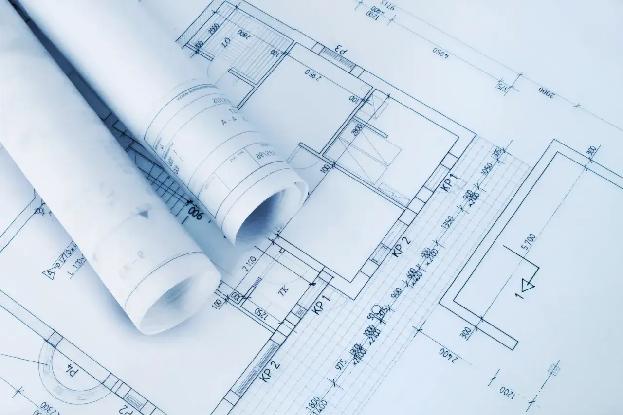Zrolowane dokumenty z projektem architektoniczno budowlanym leżą na szczegółowych planach pomieszczeń i wymiarach.