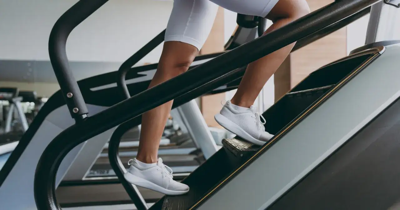 Kobieta w białych legginsach i butach sportowych wchodzi po schodach na bieżni. Czy chodzenie po schodach odchudza? Ten trening to świetny sposób na spalanie kalorii.