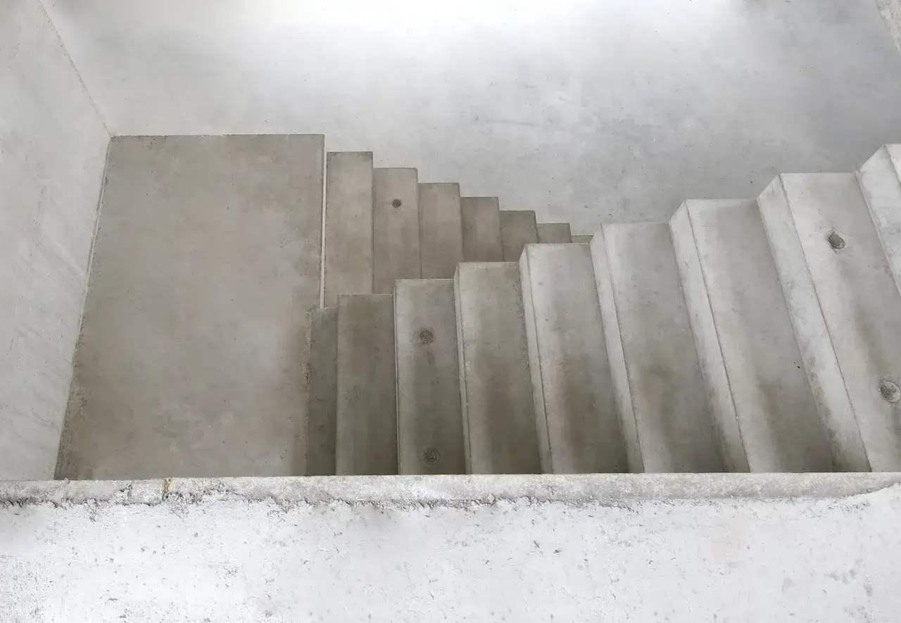 Schody betonowe prefabrykowane w surowym wnętrzu. Proste, geometryczne stopnie tworzą ścieżkę w górę.