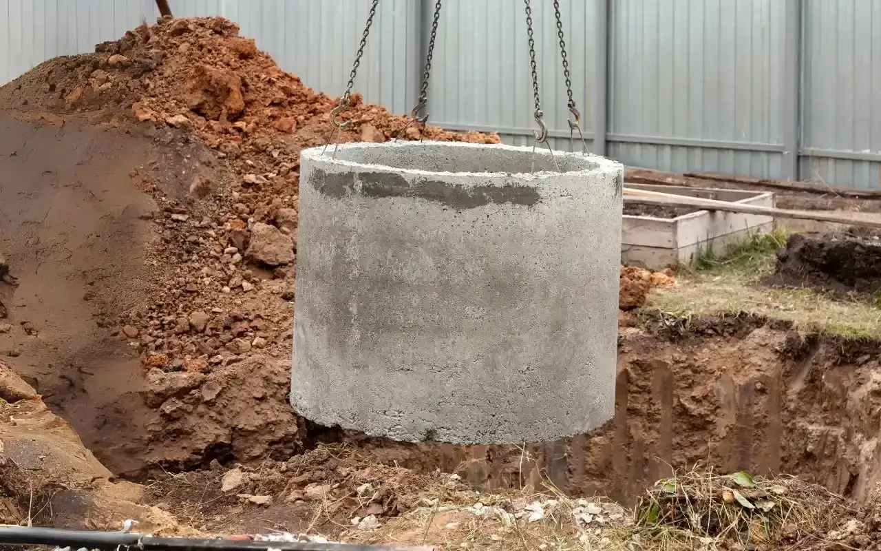 Betonowy krąg do szamba w trakcie montażu. Poznaj, ile kosztuje budowa szamba i jakie są etapy prac.