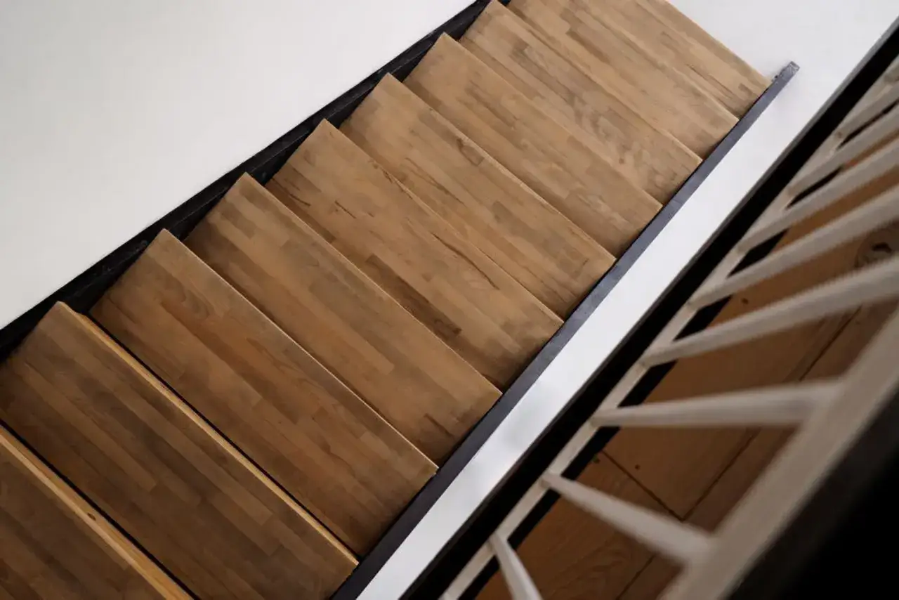 Drewniane stopnie schodów z czarną metalową konstrukcją i białymi balustradami tworzą stylowe połączenie schodów z panelami.