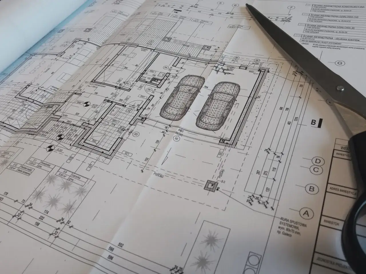 Szczegółowy projekt architektoniczno budowlany domu z garażem na dwa samochody. Nożyczki leżą na planach.